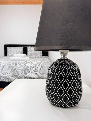 A lamp with a geometric pattern on a white surface, a bed with patterned bedding, and a plain wall in the background. - Apartment 'Mira D'Aire Serenity House Confort' (Mira de Aire)