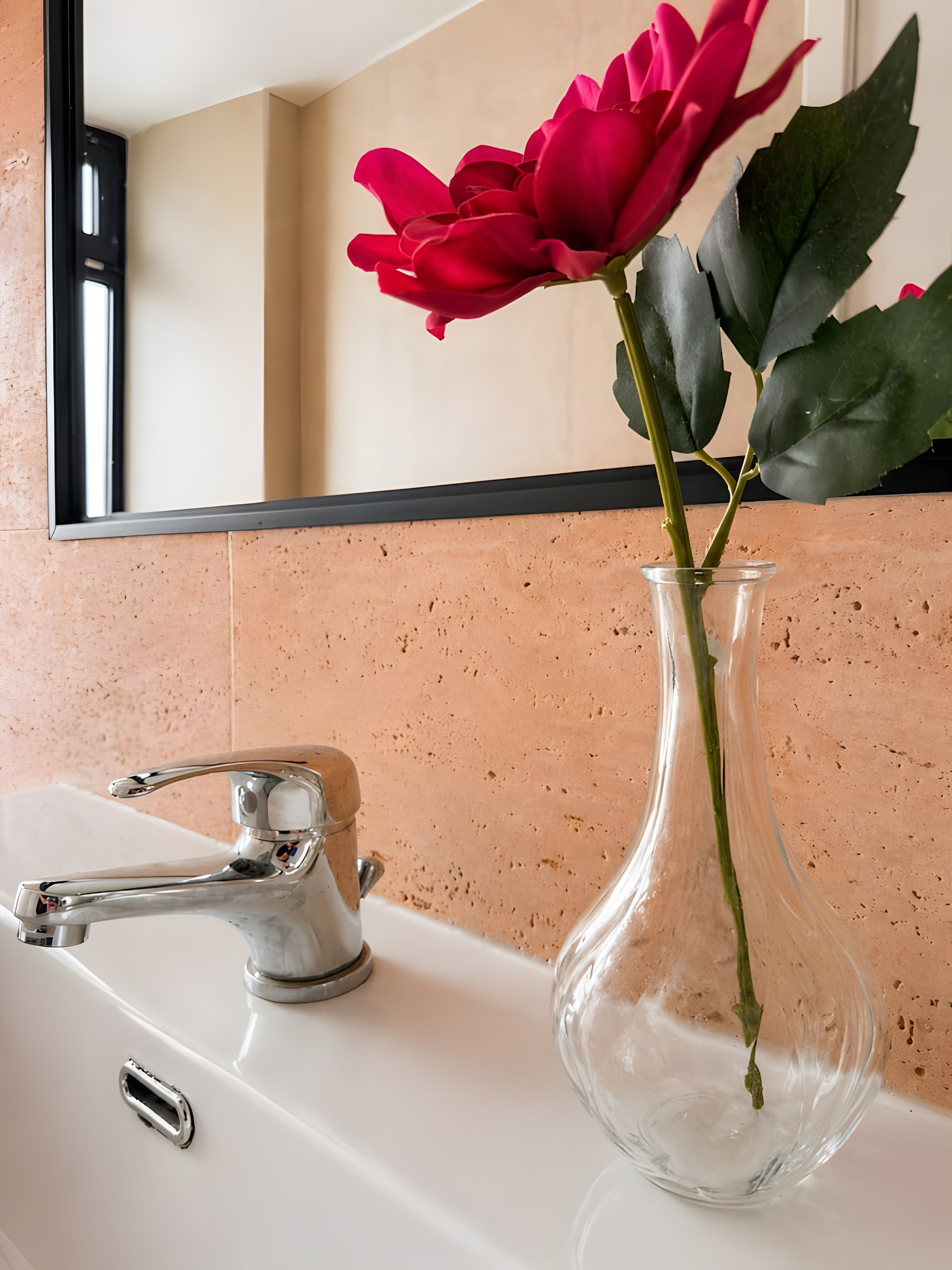 Un lavamanos de baño con una clara jarra de vidrio que contiene una sola rosa roja.