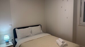 A neatly made bed with a white duvet and pillows, a bedside lamp, and a rolled towel on the bed.