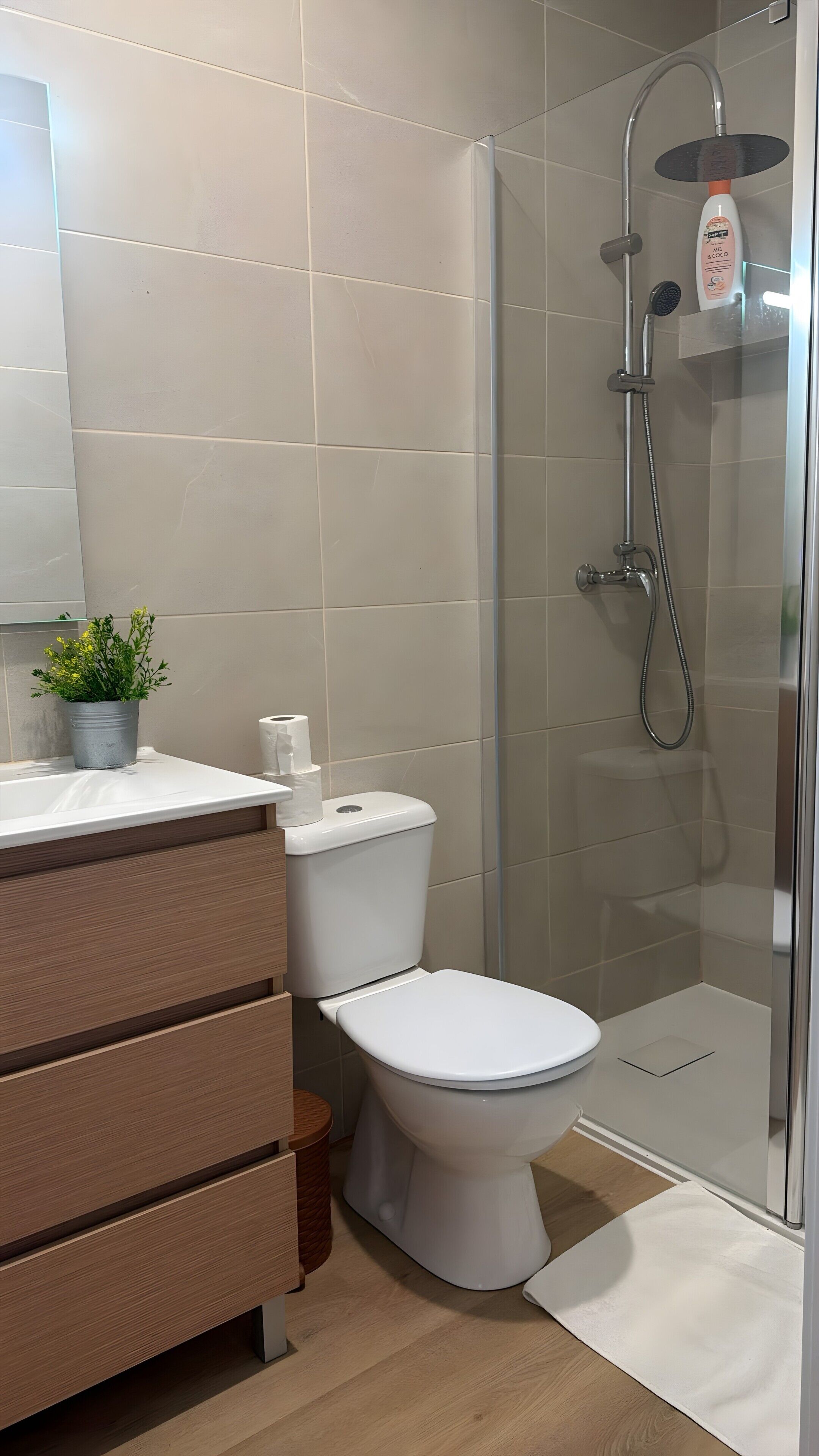 A modern bathroom with a toilet, a shower enclosure, and a vanity with a mirror.
