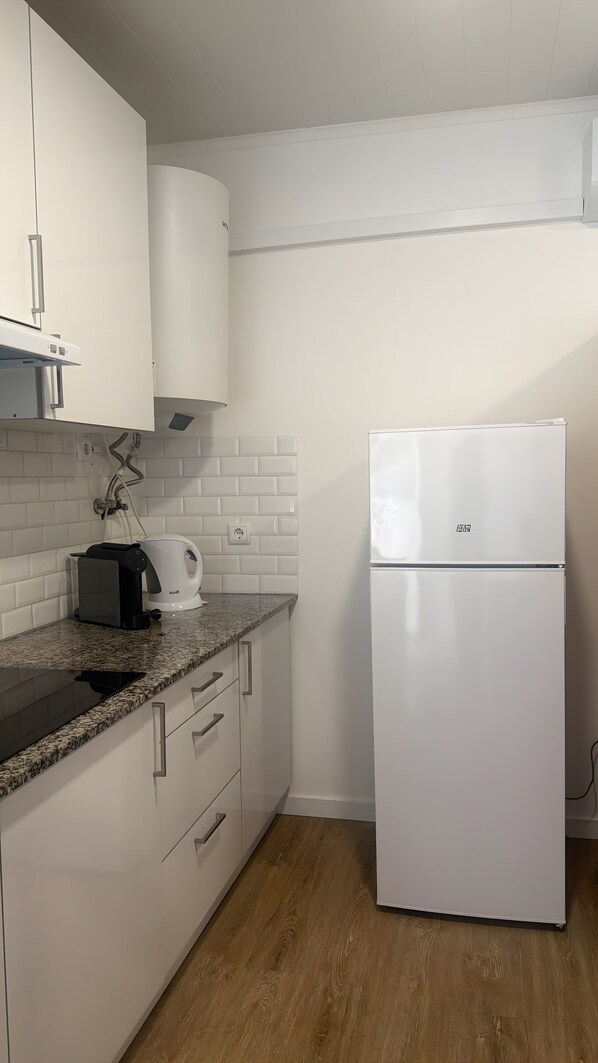 A kitchen with white cabinets, a white refrigerator, a coffee maker, and a countertop with a kettle.
