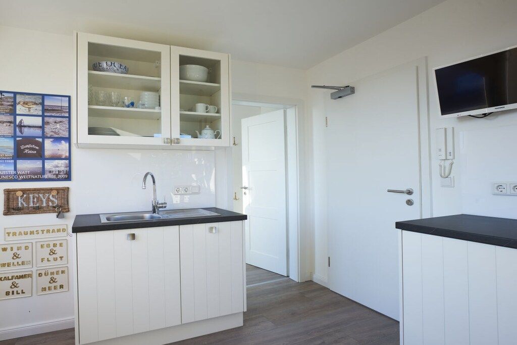 Een kleine keuken met witte kastjes, een zwart aanrechtblad en een ingebouwde televisie.