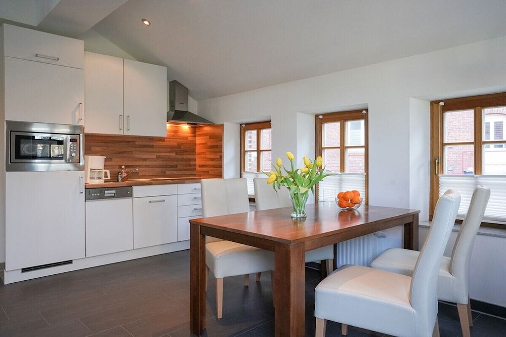 Une cuisine moderne avec des armoires blanches, un plan de travail en bois et une table à manger entourée de chaises blanches.