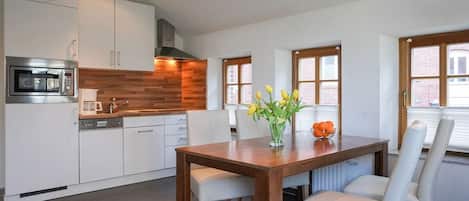 A modern kitchen with white cabinets, a wooden countertop, and a dining table with white chairs.