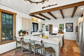 A kitchen with a central island, wooden chairs, a stove, and a refrigerator.