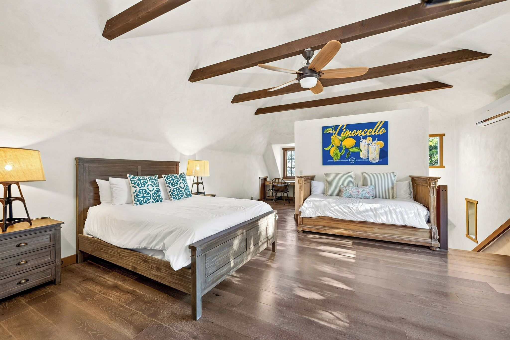 A bedroom with two beds, wooden flooring, a ceiling fan, and a wall-mounted artwork.