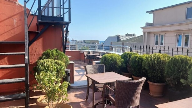Eine Dachterrasse mit Gartenmöbeln, Blumentöpfen und Blick auf die Stadtlandschaft.