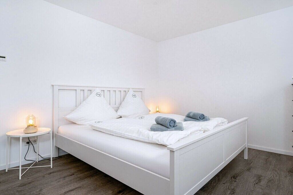 Un lit blanc avec une tête de lit, deux tables de chevet et une petite table de nuit avec une lampe.