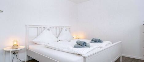 A white bed with a headboard, two bedside tables, and a nightstand with a lamp.