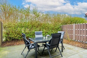 Eine Terrassenanlage mit Tisch und vier Stühlen, die Tischplatte ist aus Glas.