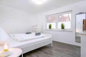 Ein Schlafzimmer mit Bett, Nachttisch und einem Fenster mit Pflanzen.