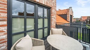 A brick building with large windows, a balcony with a table and chairs, and a view of neighboring houses. - Holiday apartment with 1 bedroom (Greetsiel)