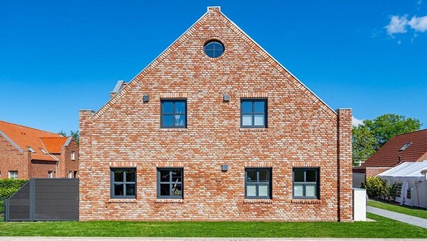 A brick building with a triangular roof, multiple windows, and a small circular window on the roof. - Holiday apartment with 1 bedroom (Greetsiel)