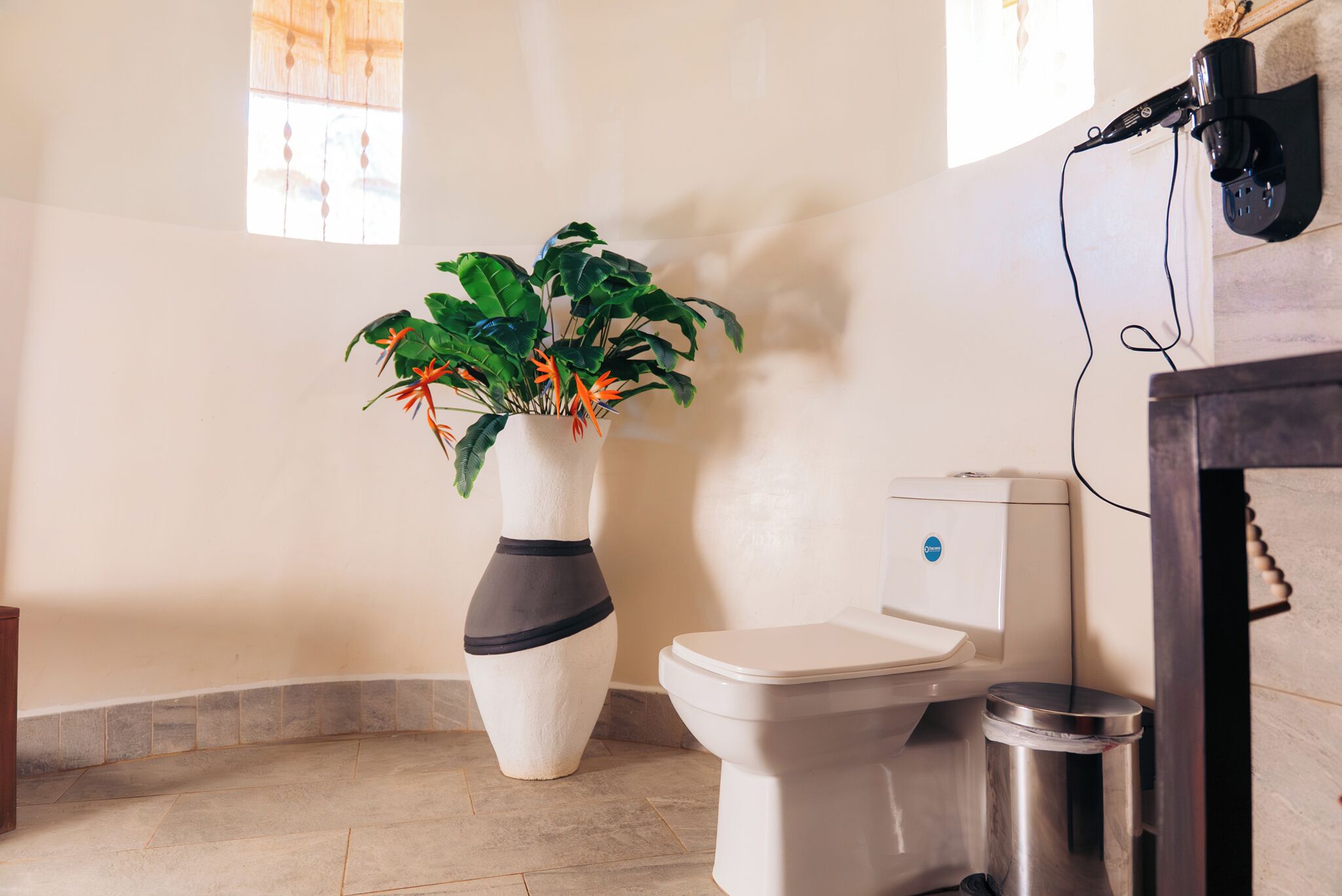 Une salle de bain avec des toilettes, une poubelle, un lavabo et une plante en pot.