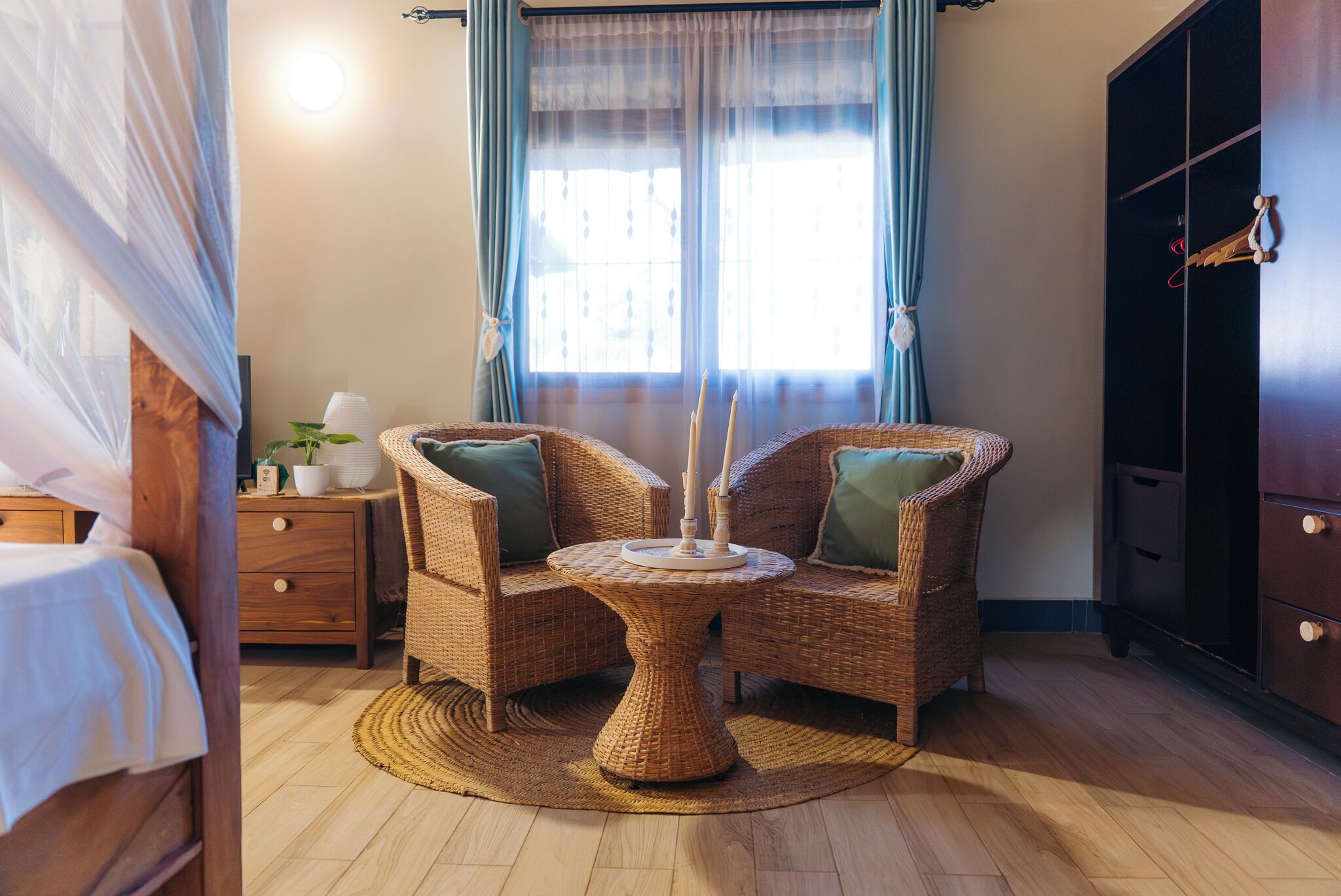 A room with a bed, a nightstand, a wicker chair, a round table, and a wardrobe.