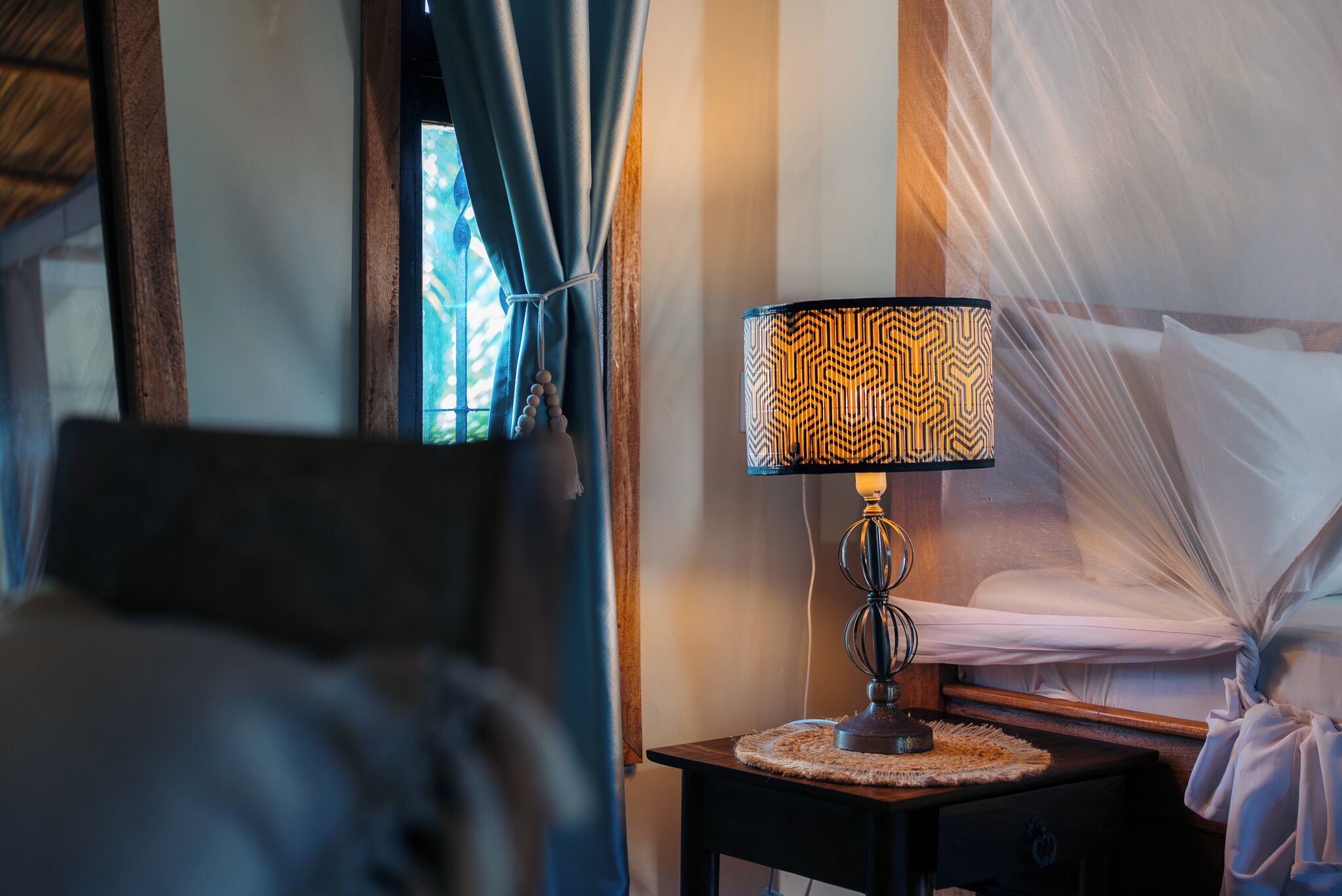 A hotel room with a bed, a nightstand with a lamp, and a window with curtains.