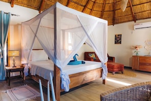 A room with a four-poster bed, a wooden nightstand, a lamp, a red chair, a wooden dresser, and a woven rug. - Spacious Villa, 2-Min Beach Walk - AC, Wifi (Pwani Mchangani)