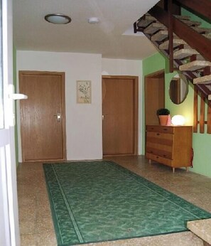 A hallway with wooden doors, a green patterned rug, and a wooden dresser with a mirror.