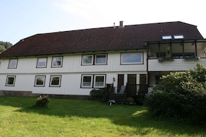A two-story house with a sloped roof, multiple windows, a front porch, and a small garden area. - Holiday apartment with 1 bedroom (Osterode - Lerbach)