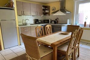 Een keuken met een eettafel, stoelen, een koelkast, een magnetron en een fornuis.