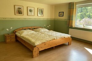 A bedroom with a wooden bed, a nightstand, a window with curtains, and wall-mounted pictures. - Holiday apartment with 1 bedroom (Osterode - Lerbach)
