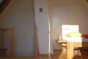 Ein Schlafzimmer mit schrägem Dach, einem Bett mit gelbem Kopfkissen, einem Nachttisch mit Lampe und einem kleinen Fenster.