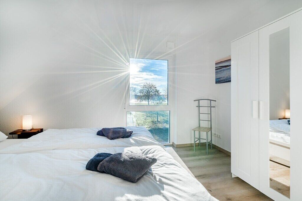 Une chambre avec deux lits, une grande fenêtre donnant sur les arbres, une armoire et une table de chevet avec une lampe.
