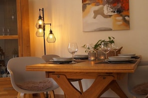 A dining area with a wooden table set for two, two chairs, a wall-mounted light fixture, and a painting. - Holiday apartment with 3 bedrooms (Munster)