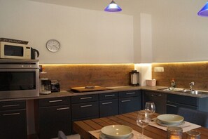 Eine moderne Küche mit dunklen Schränken, einer Holz Arbeitsplatte, einer Mikrowelle, einer Kaffeemaschine und einer Uhr an der Wand.