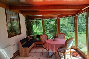 Ein Zimmer mit Holzwänden, einem Tisch, Stühlen und einer Bank, mit Blick auf Grünflächen.