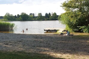 Eine Uferlandschaft mit Sandstrand, einer Holzsteganlage und einem Picknickplatz.