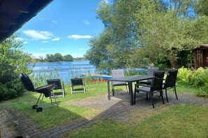 Ein Essbereich im Freien mit Tisch und Stühlen, einem Grill und Blick auf einen See.