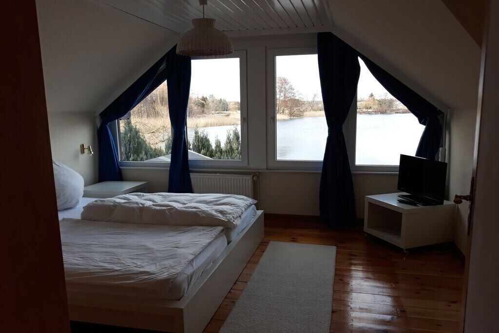 A bedroom with a bed, a television on a stand, and a view of a lake through large windows.