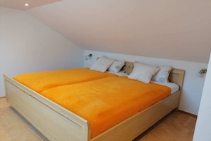 Ein Einzelbett mit Holzrahmen und einer leuchtend orangefarbenen Tagesdecke in einem Zimmer mit weißen Wänden und einer geneigten Decke.