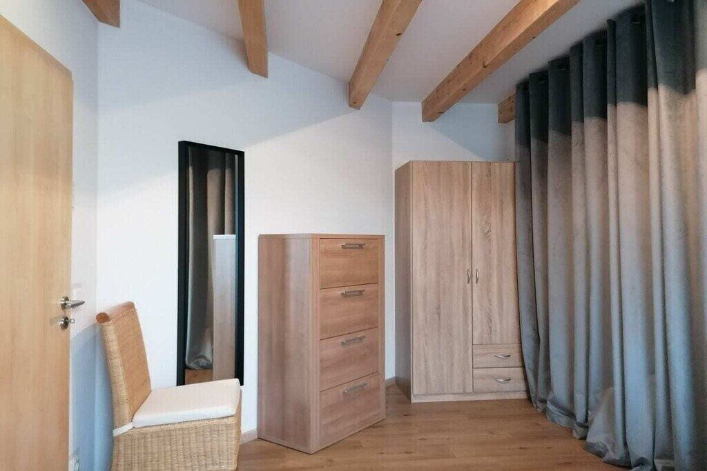 A room with a wooden floor, a wooden wardrobe, a chair, and a door.