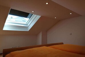 Ein Schlafzimmer mit Dachfenster, einem Bett und einer Decke mit Einbauleuchten.