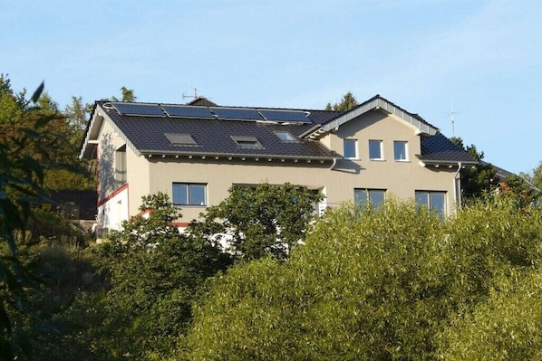 Ein zweistöckiges Gebäude mit geneigtem Dach, Solaranlagen und zahlreichen Fenstern.