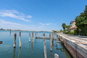Une propriété située au bord de l’eau, dotée d’un quai s’étendant dans une zone d’eau calme, d’une promenade pavée et d’un bâtiment avec un toit rouge.