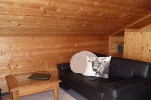 A log cabin interior with a black leather sofa, a wooden coffee table, and a pillow with a cow print. - Fellhorn in the Auffenberg guesthouse (Fischen)