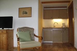A compact living space with a wooden chair, a television, a framed picture, and a kitchenette. - Fellhorn in the Auffenberg guesthouse (Fischen)