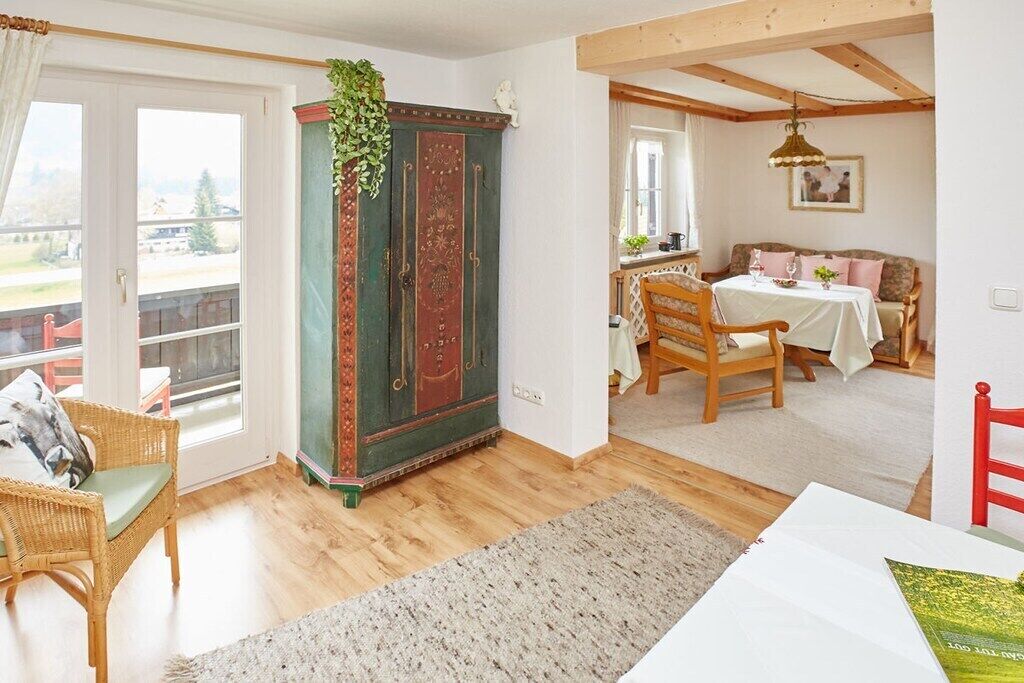 A room with a wooden floor, a green cabinet with red doors, a wicker chair, a dining table with chairs, and a view through a glass door.