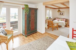 Een kamer met een houten vloer, een groen kastje met rode deuren, een rieten stoel, een eettafel met stoelen en uitzicht door een glazen deur.