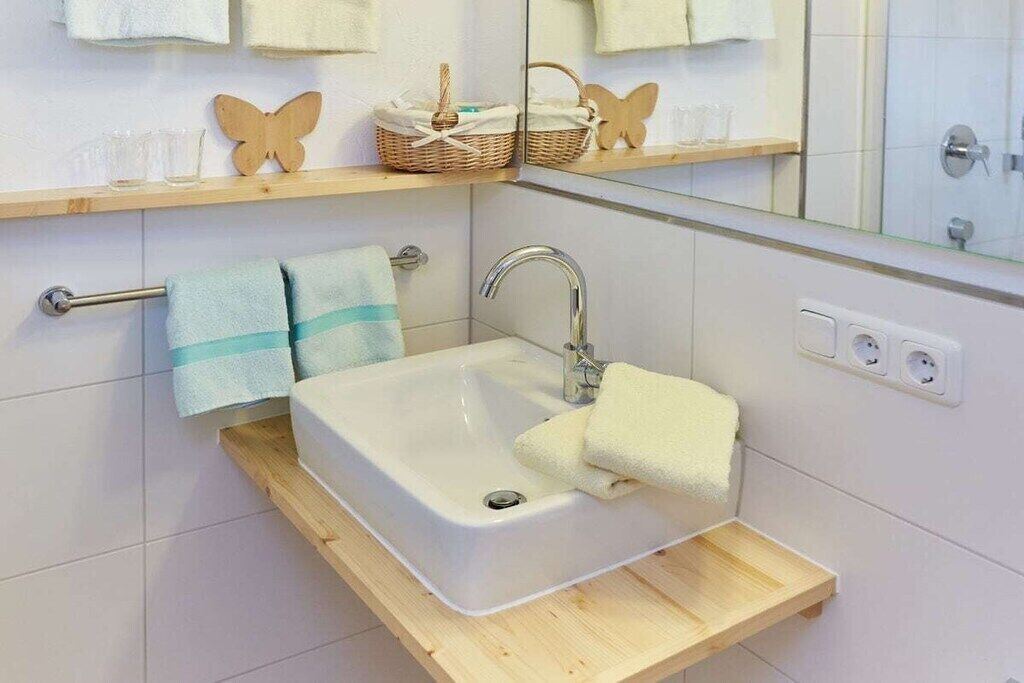 Une salle de bain avec un lavabo blanc, un miroir, un porte-serviettes et une étagère sur laquelle se trouvent un panier et des verres.