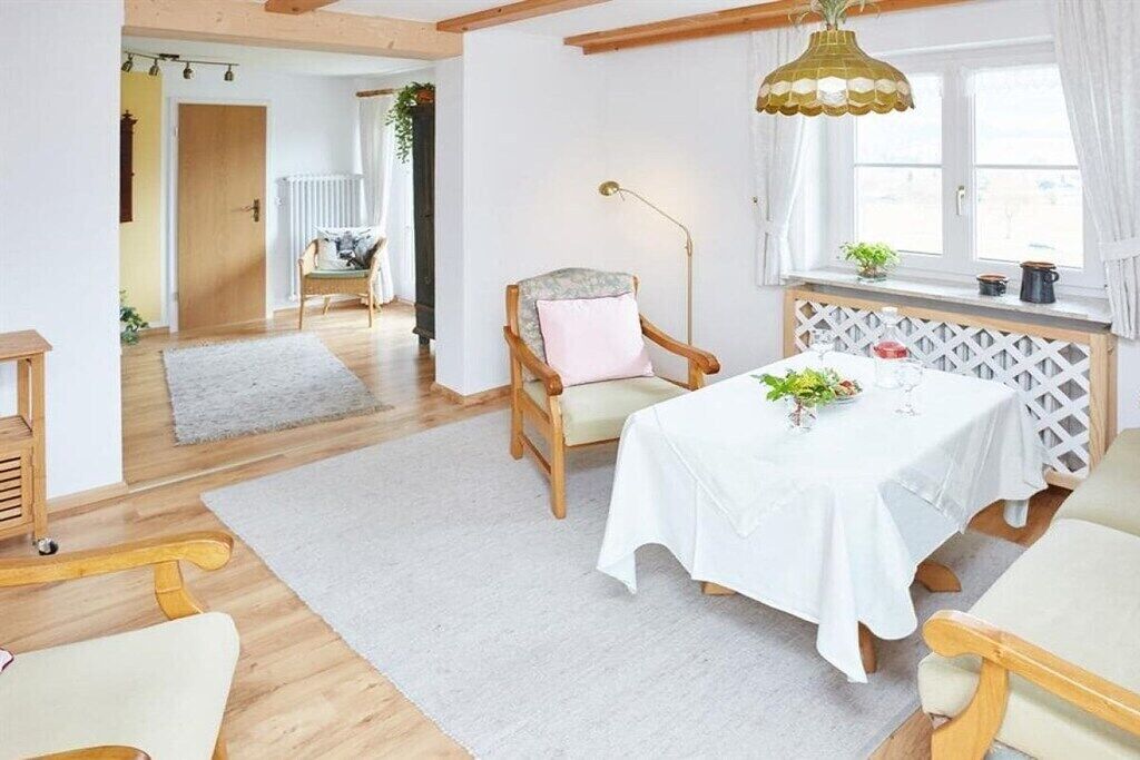 Ein Zimmer mit Esstisch, gedeckt für zwei Personen, einem Holzstuhl, einer Stehlampe und einem Fenster mit Vorhängen.