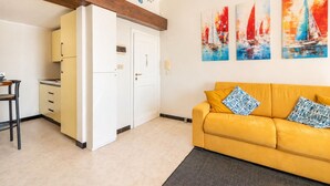 Una sala de estar con un sofá amarillo, un área de cocina con gabinetes amarillos y una puerta que da a otra habitación.
