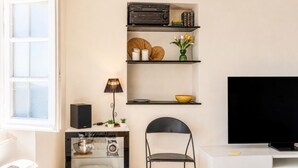 Una sala moderna con un televisor de pantalla plana, un sillón negro, un mueble blanco y una estantería con libros y objetos decorativos.