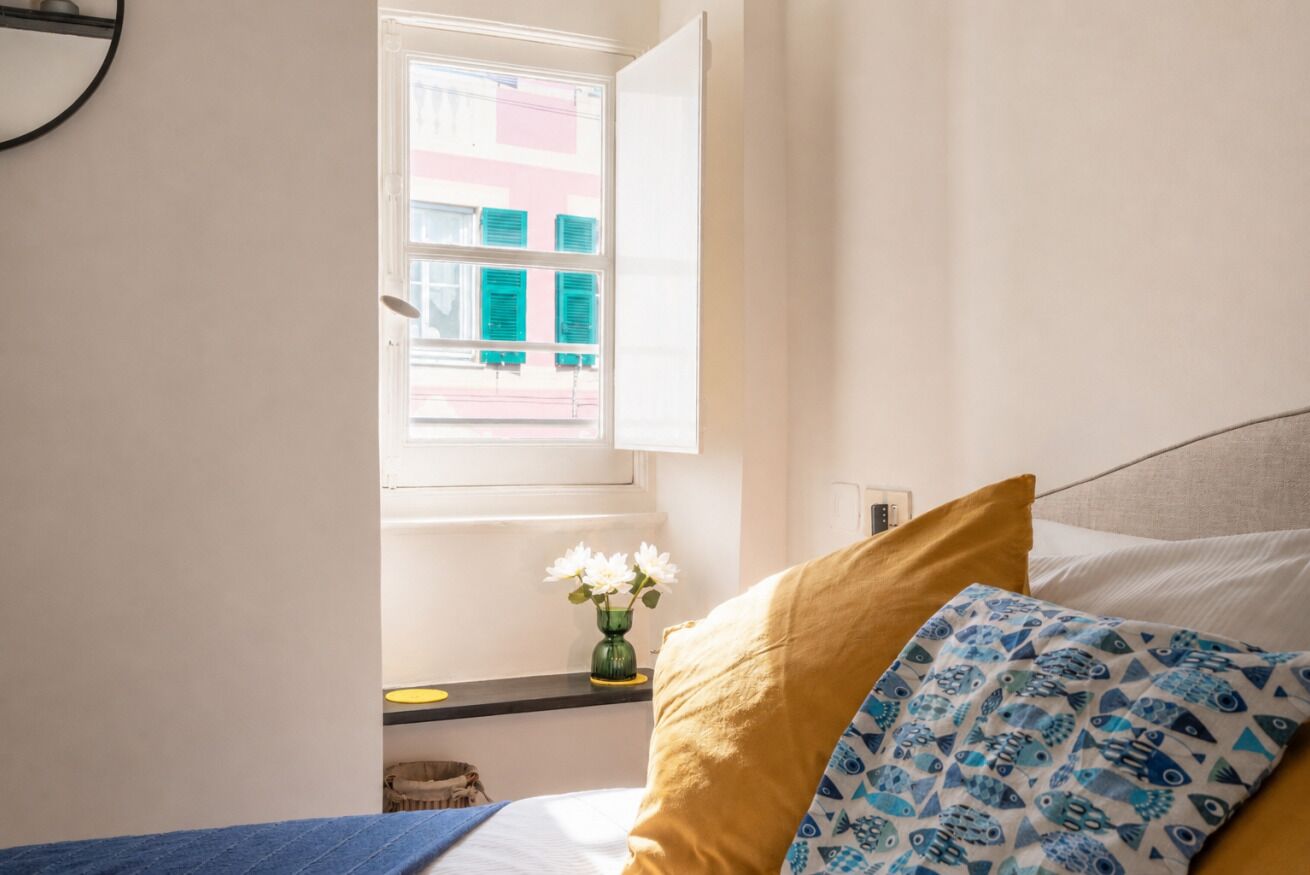 A bedroom with a bed, a window, and a vase with flowers.