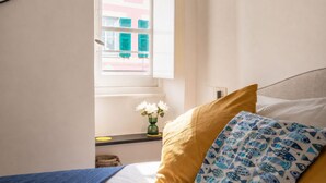 Un dormitorio con cama, ventana y un jarrón con flores.