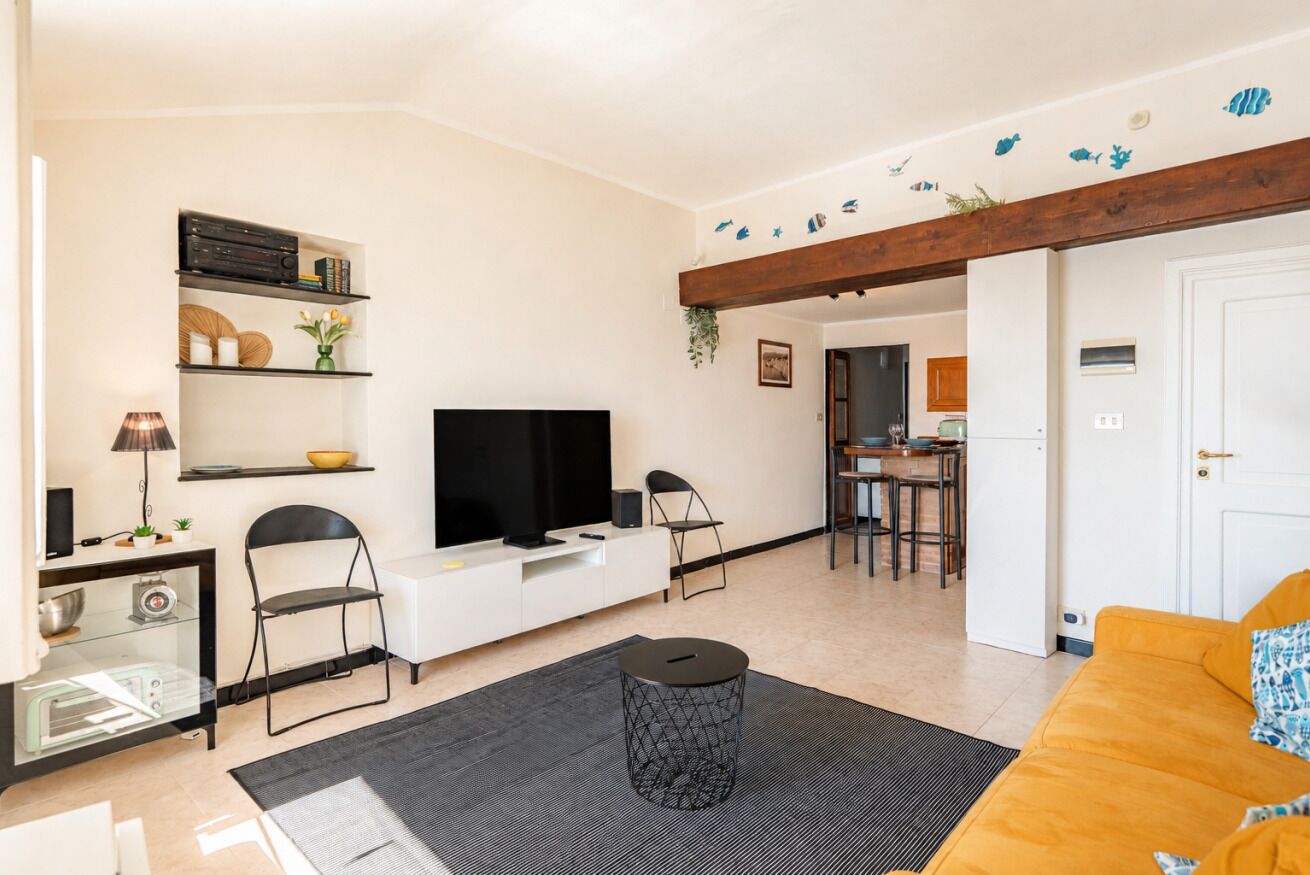 A modern living room with a flat-screen TV, a sofa, a coffee table, and a dining area with a kitchen in the background.