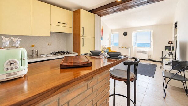 Una cocina con isla de madera, estufa a gas y un tostador antiguo. Hay una zona de comedor con mesa y sillas.